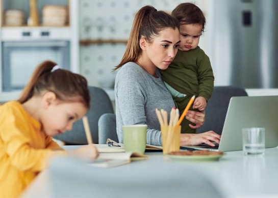 Mother uses laptop with kids at the dining room table.